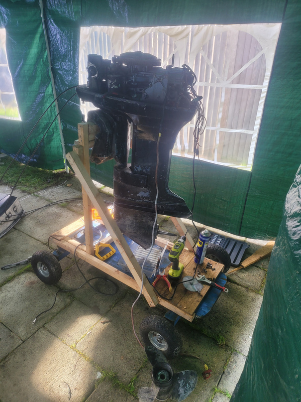 The outboard motor stripped and on a homemade wheeled stand for teardown