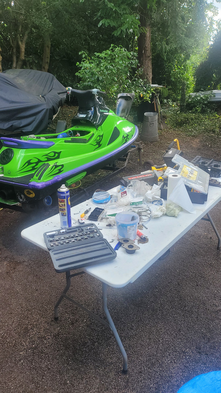 The green Kawasaki jet ski in the garden with a bench of parts laid out next to it